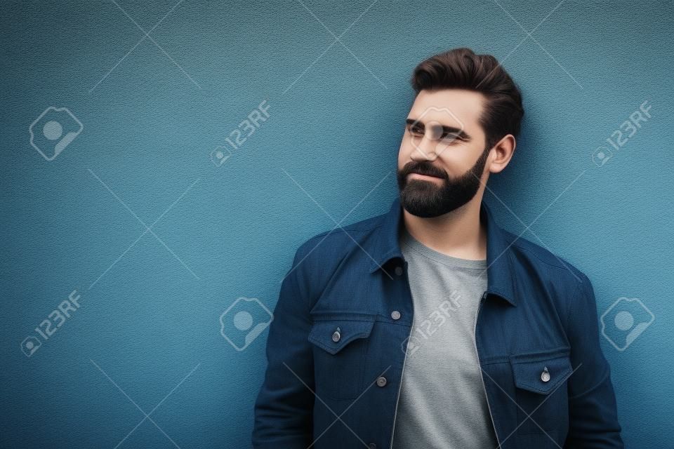 Handsome bearded man leaning to gray wall outdoors. Space for text