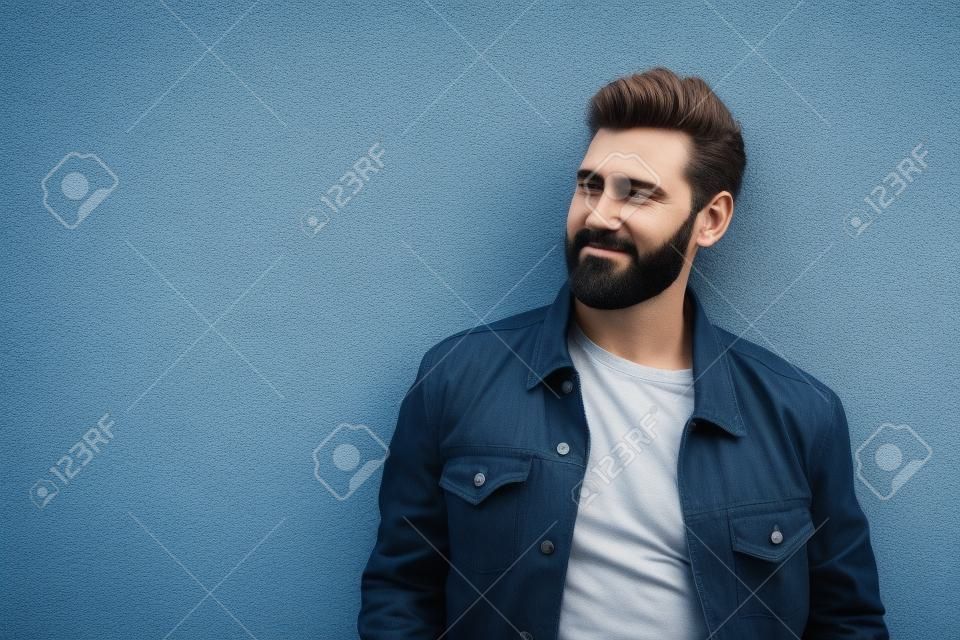 Handsome bearded man leaning to gray wall outdoors. Space for text