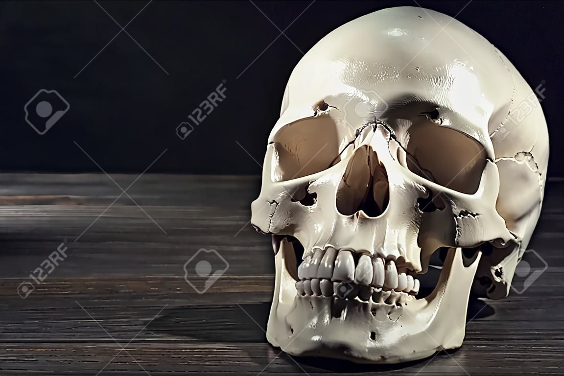 Human skull on wooden table against black background, space for text