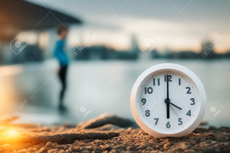 Woman doing morning exercises near river outdoors, focus on alarm clock