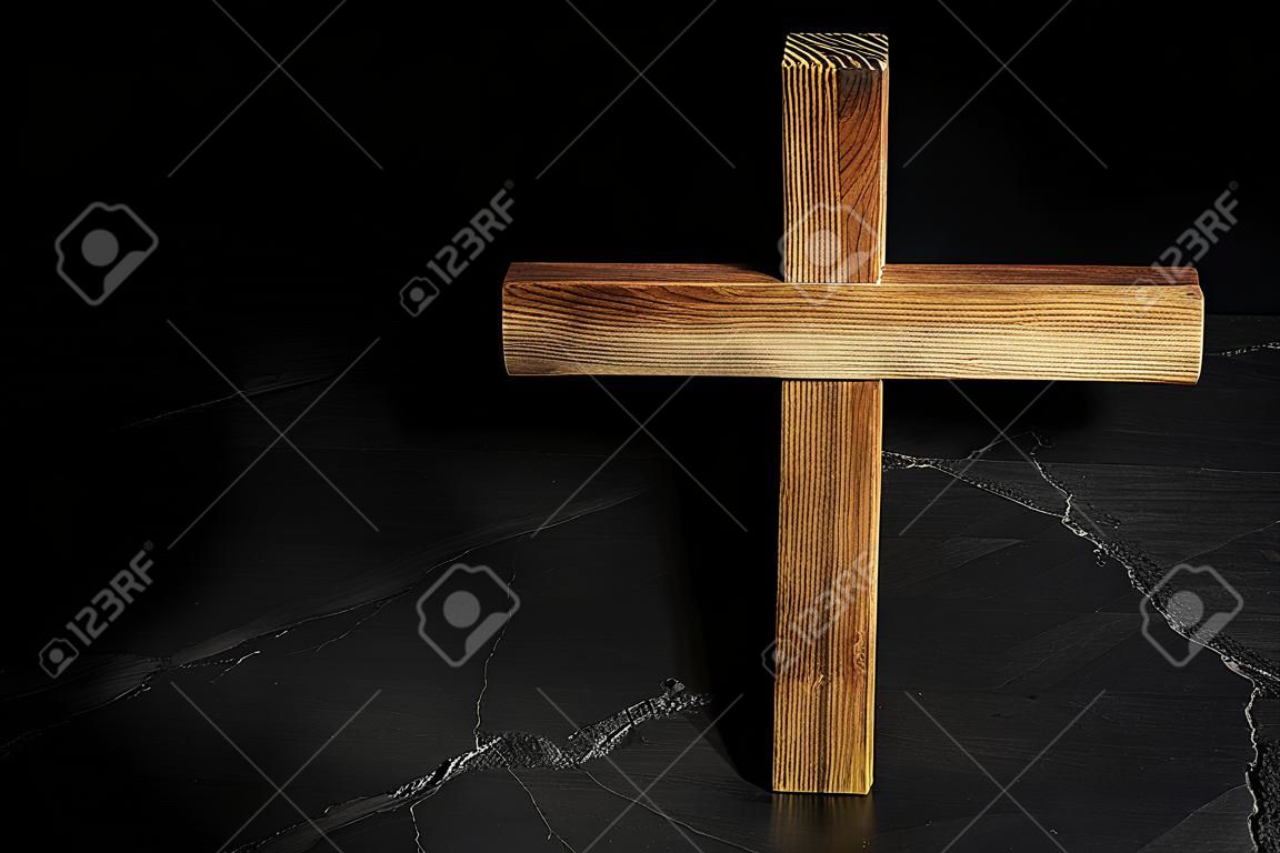 Wooden Christian cross on black slate table against dark background, above view with space for text. religion concept