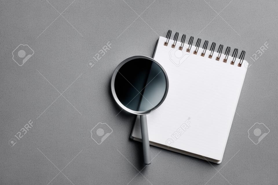 Top view of magnifier glass and empty notebook on light gray stone background, space for text. Find keywords concept