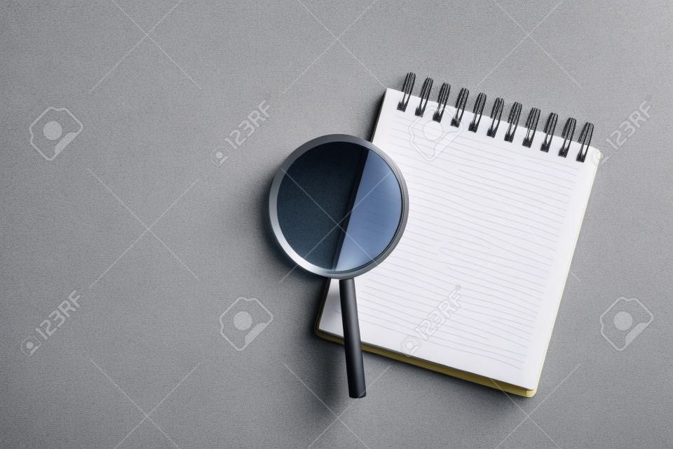 Top view of magnifier glass and empty notebook on light gray stone background, space for text. Find keywords concept