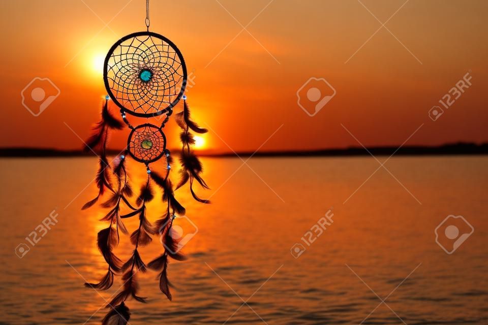 Beautiful handmade dream catcher near river at sunset. Space for text  Photos