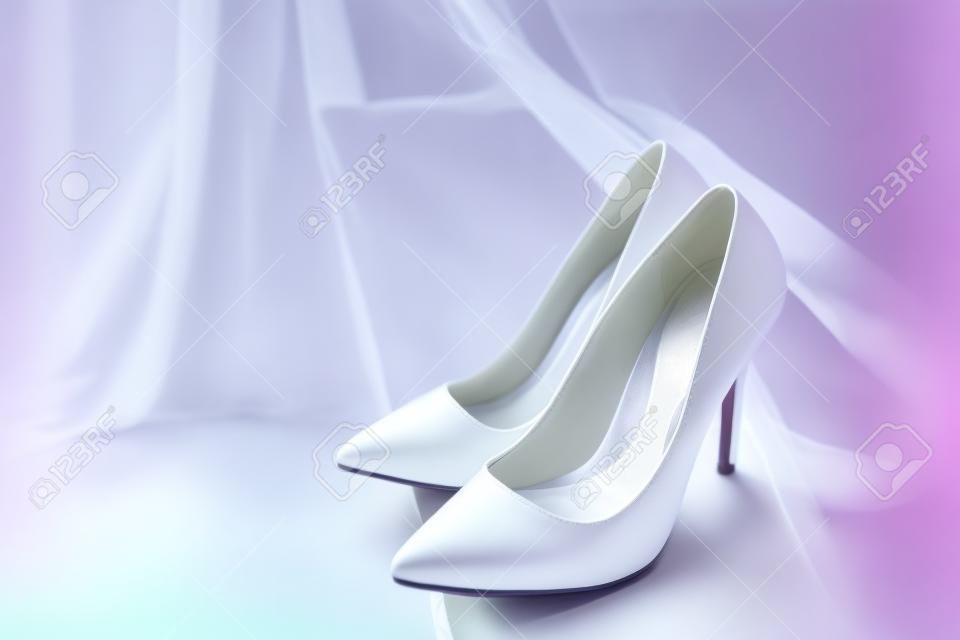 Paar weiße Schuhe mit hohen Absätzen und verschwommenes Hochzeitskleid auf Hintergrundfläche für Text