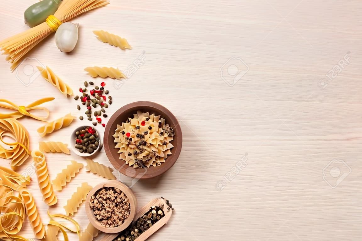 Flat lay composition with different types of pasta on light wooden table, space or text