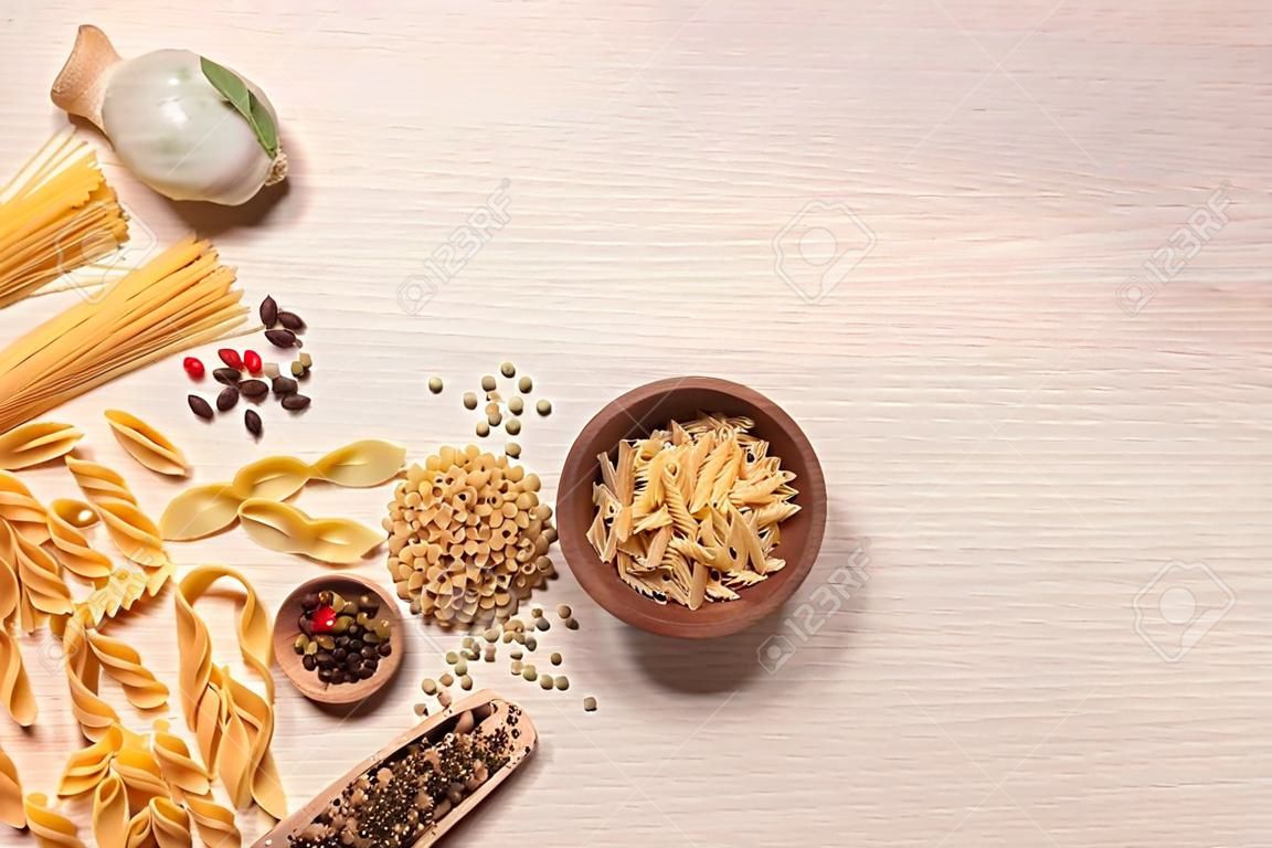 Flat lay composition with different types of pasta on light wooden table, space or text