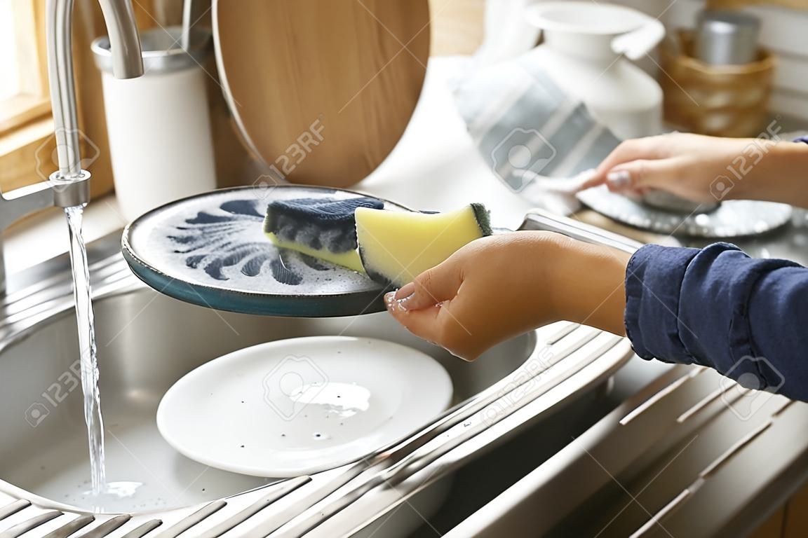 Woman washing plate in kitchen sink, closeup