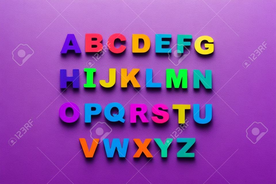 Colorful magnetic letters on violet background, flat lay. alphabetical order