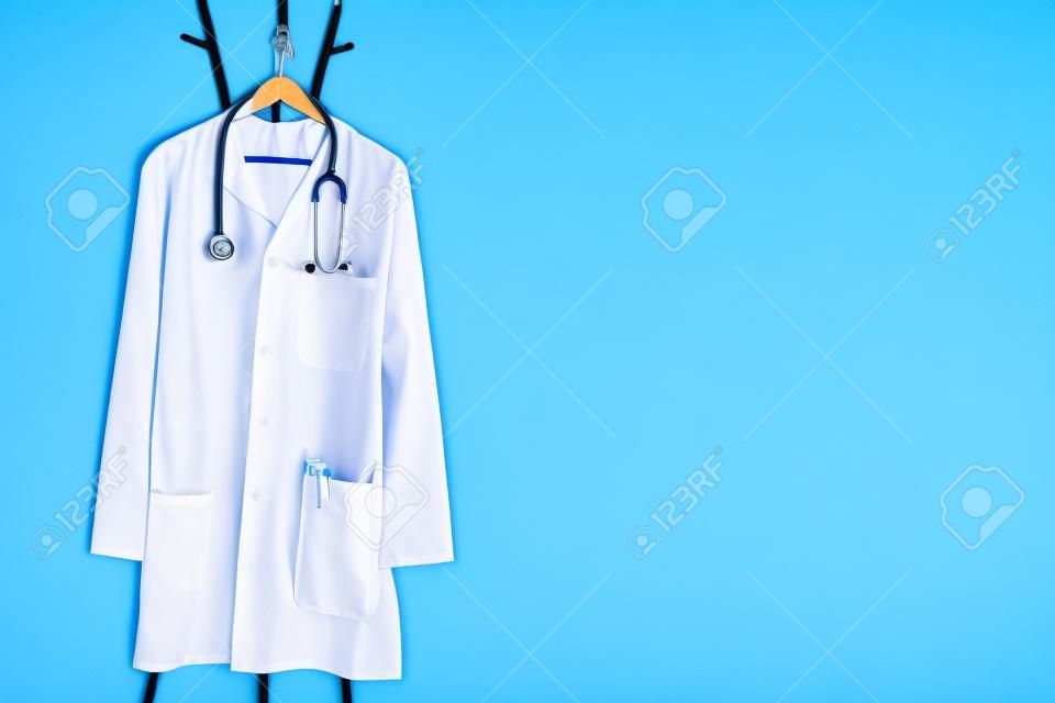 White medical uniform and stethoscope hanging on rack against light blue background. Space for text
