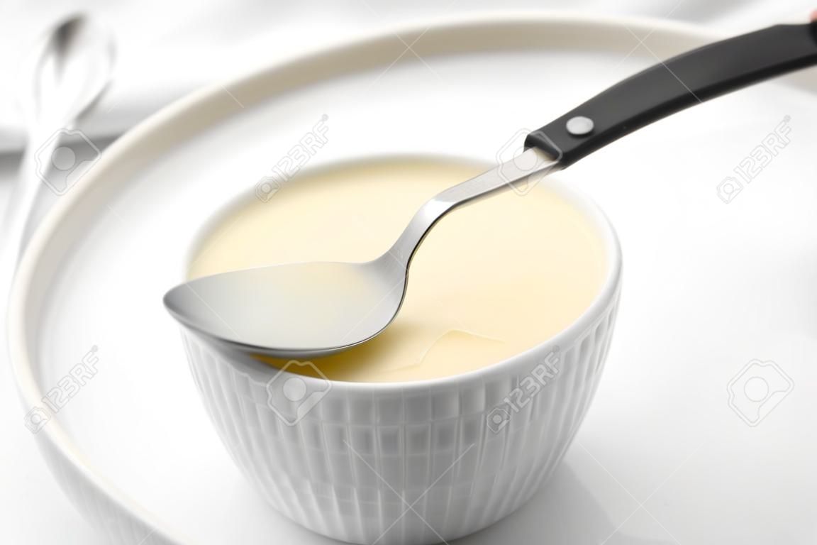 Bowl with condensed milk and spoon on white table, closeup