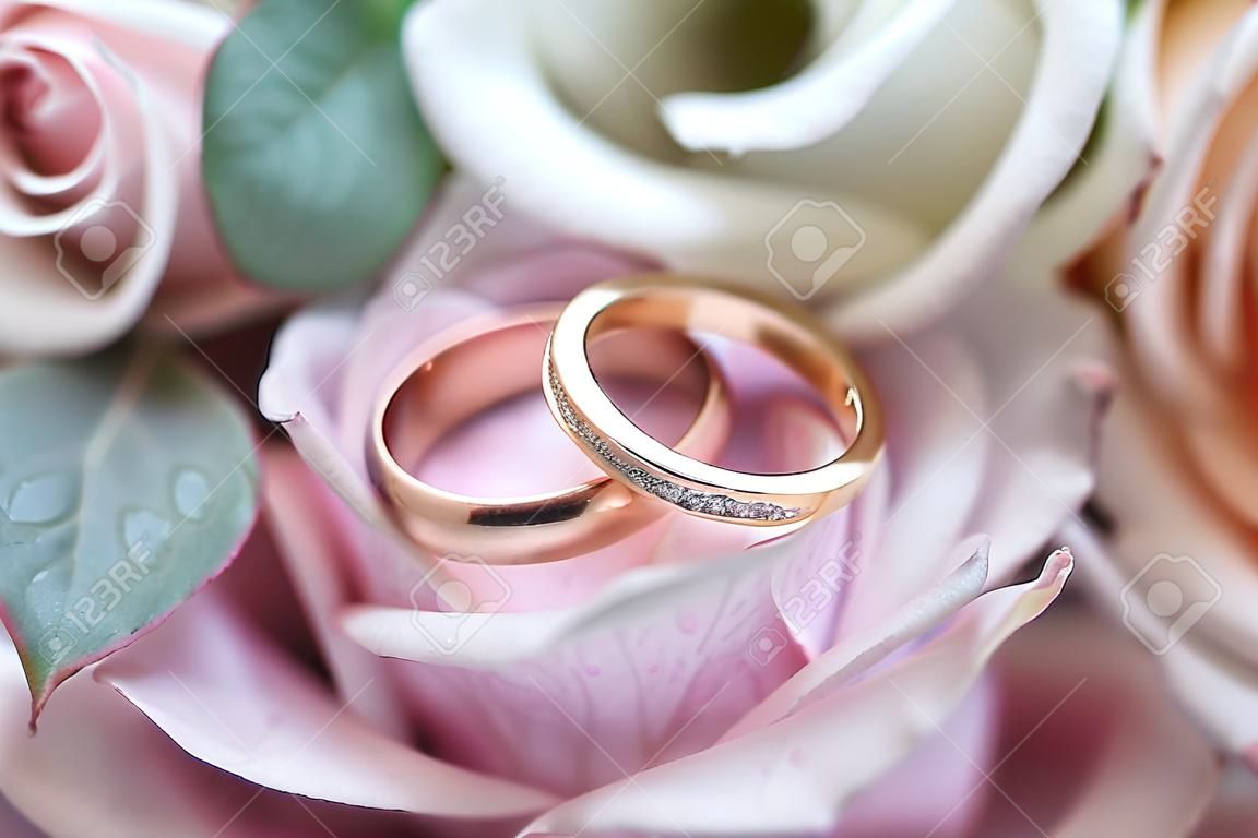 Fedi nuziali d'oro su un bouquet da sposa di rose rosa