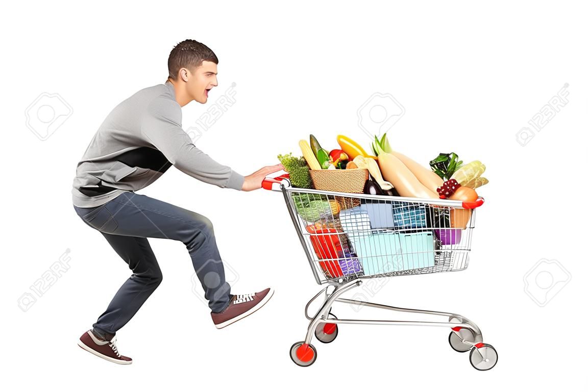 若い男を実行していると、白い背景で隔離された食物と一緒に完全ショッピングカートを押す