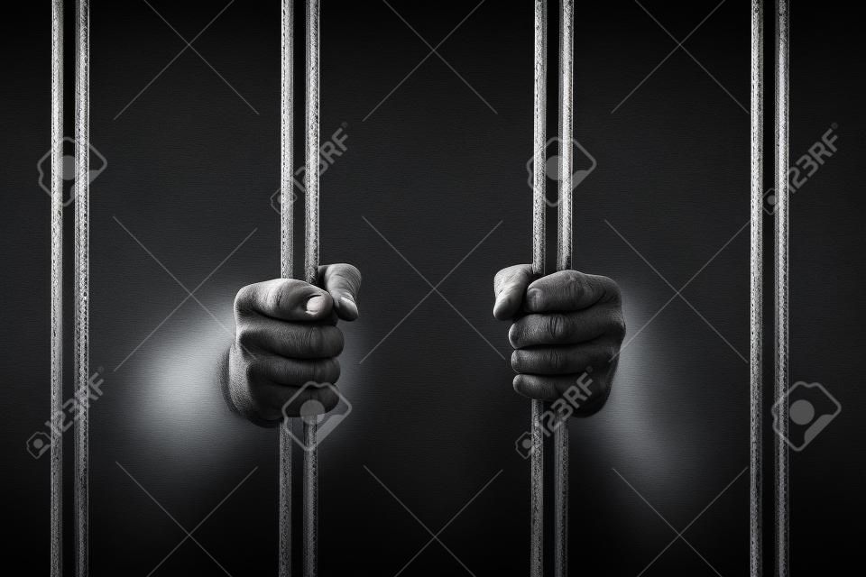 Мужской руки держат в тюрьмах бары, изолированных на черном фоне