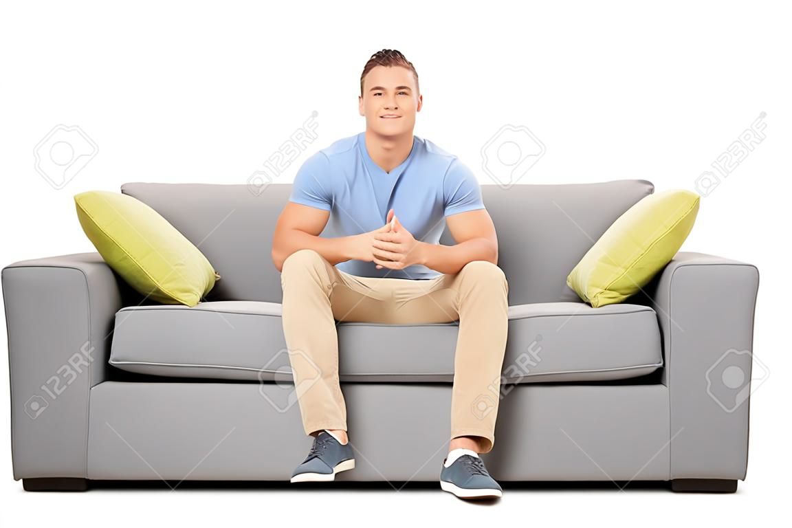 Apuesto joven sentado en un sofá moderno aislado en el fondo blanco