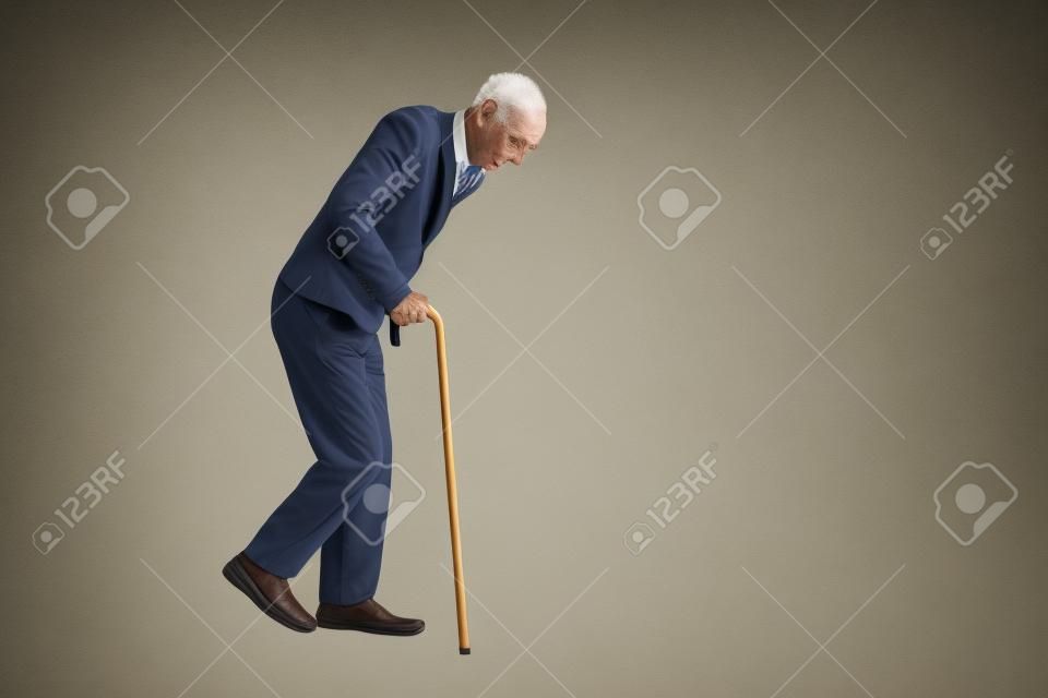 Studio foto de un anciano agotado caminando con un bastón aislado en el fondo blanco