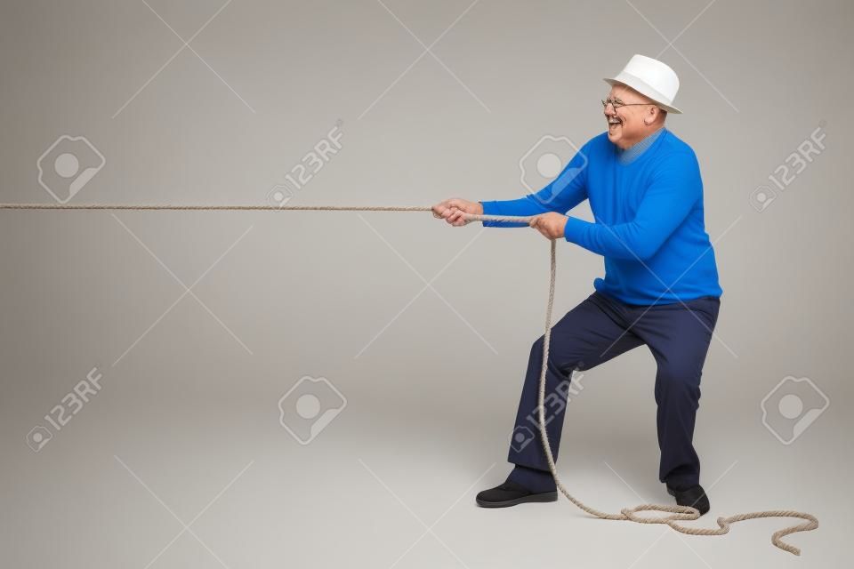 Foto de estúdio de um idoso alegre puxando uma corda isolada no fundo branco