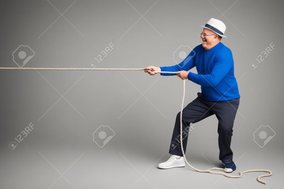 Studio opname van een vrolijke senior trekken van een touw geïsoleerd op witte achtergrond