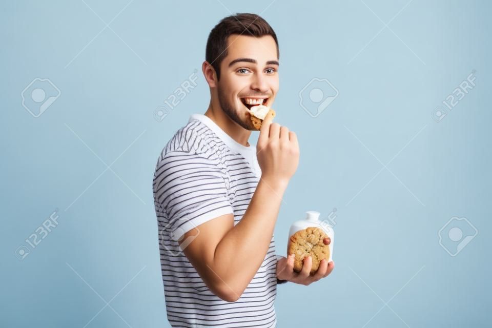 年轻人吃着饼干，拿着一个白色背景下的饼干罐。
