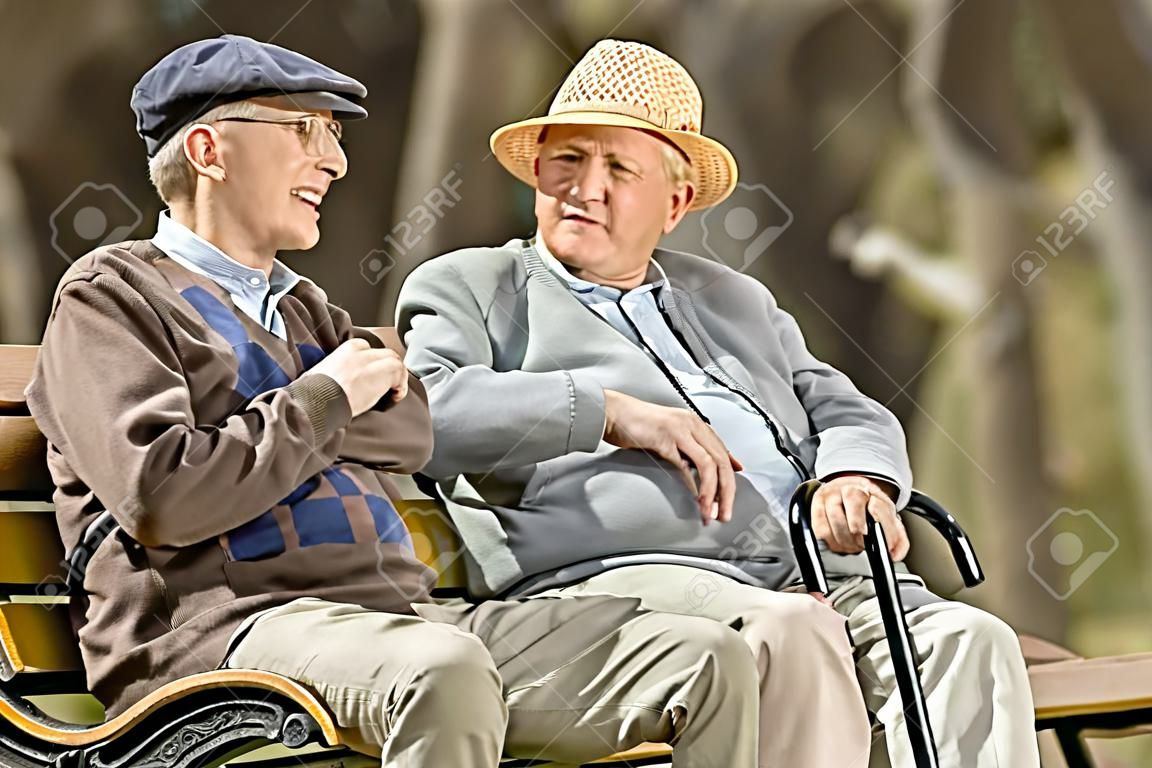 Two elderly men seated on a bench talking with each other outdoors