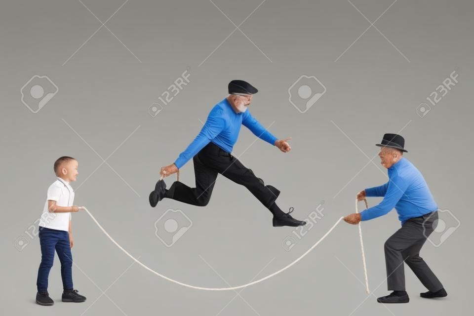 Full length profile shot of a grandfather and grandson holding a rope and an elderly man skipping isolated on white background