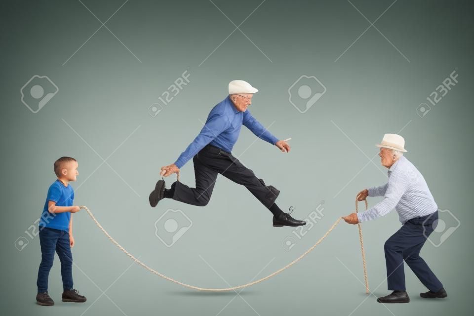 Colpo di profilo integrale di un nonno e di un nipote che tengono una corda e un uomo anziano che salta isolato su sfondo bianco