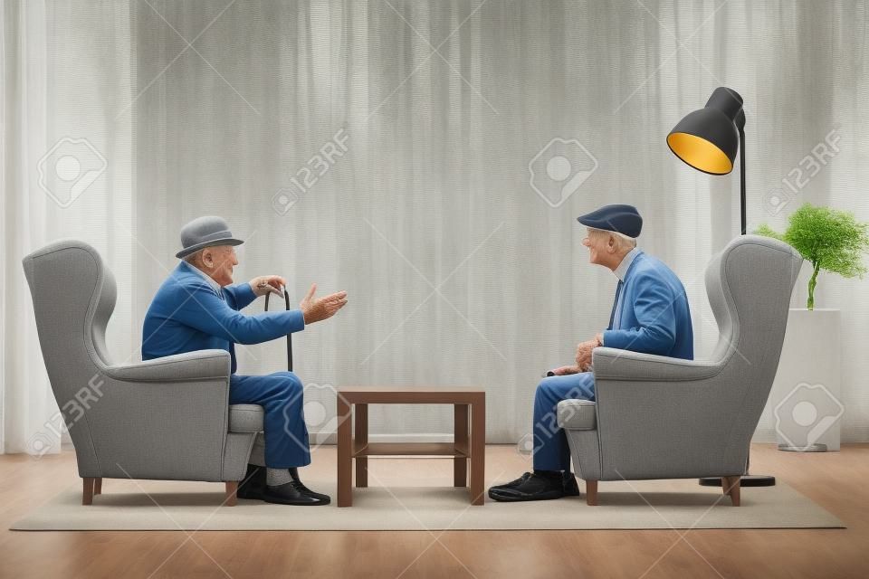 Dwóch starszych mężczyzn siedzących w fotelach i rozmawiających w pokoju