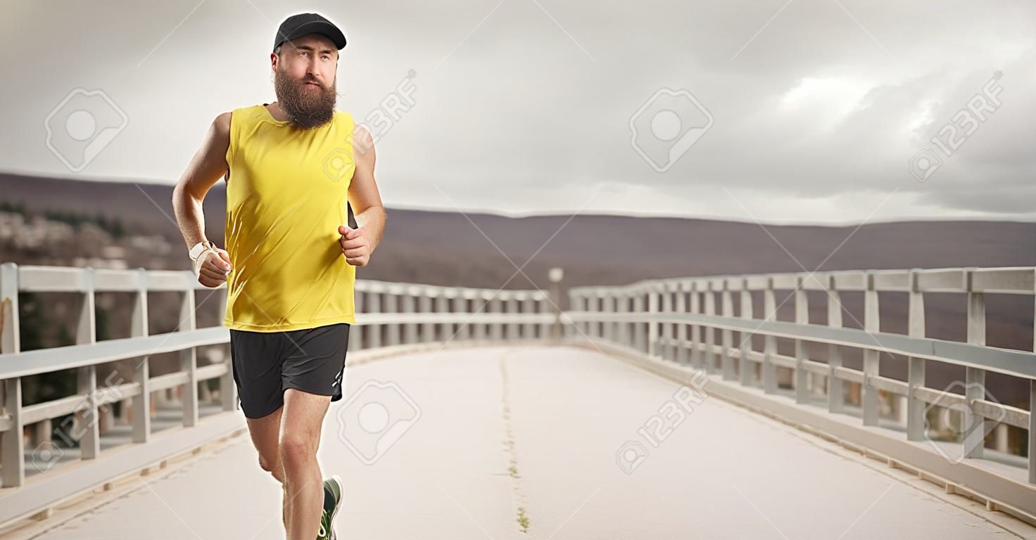 Homme barbu avec une casquette faisant du jogging sur un pont