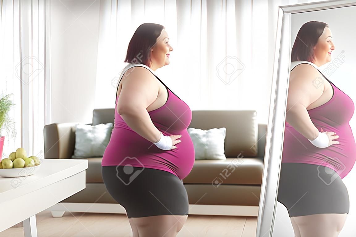 Plus size woman in sportswear looking at her reflection in a mirror at home