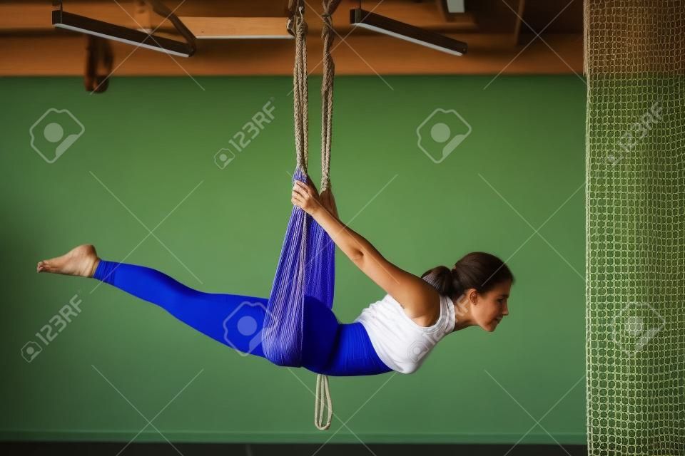 Una donna appesa a un'amaca appesa fa yoga in palestra.