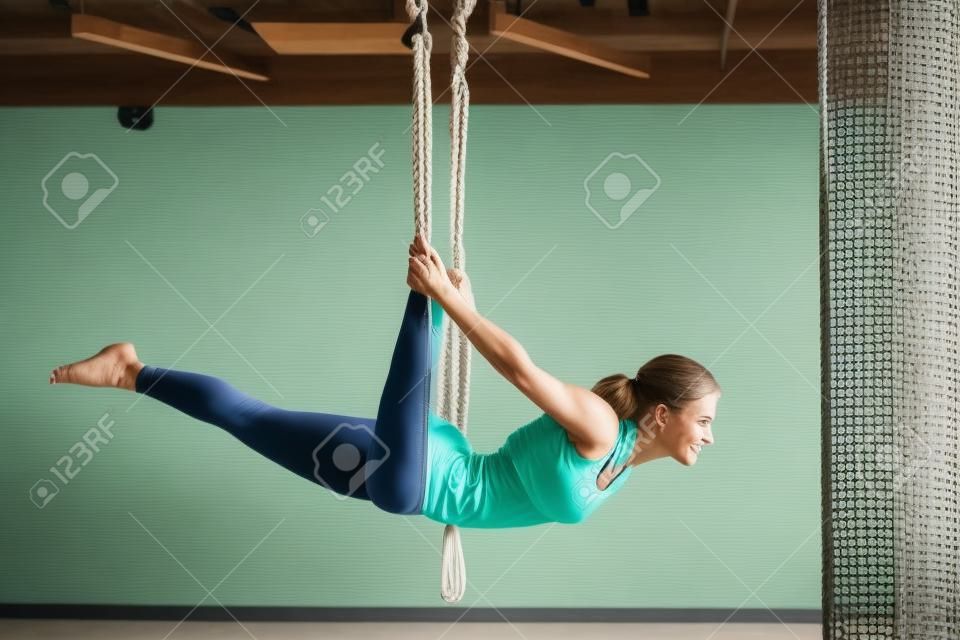 Una donna appesa a un'amaca appesa fa yoga in palestra.