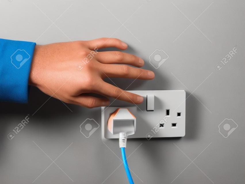 Eine männliche Hand, drückt einen Schalter an eine Steckdose