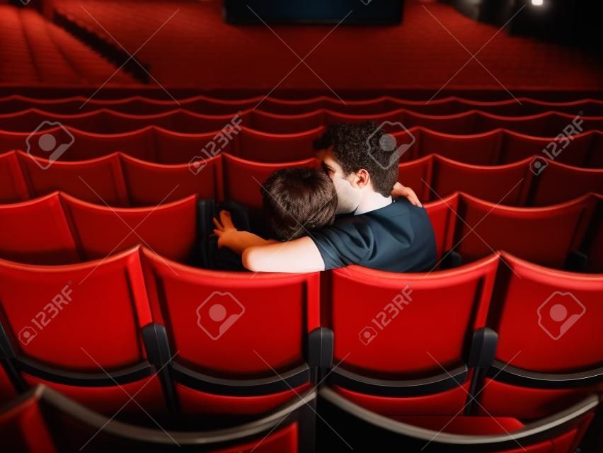 Vista posterior disparo de una pareja de jóvenes sentados en una sala de cine y besos