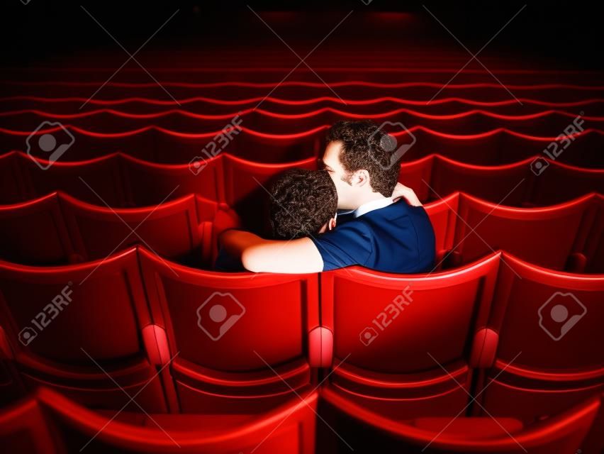 Vista posterior disparo de una pareja de jóvenes sentados en una sala de cine y besos