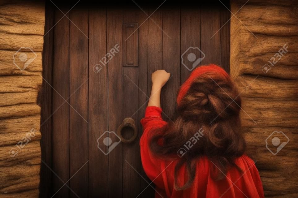 Une jeune femme frappe sur une vieille porte en bois