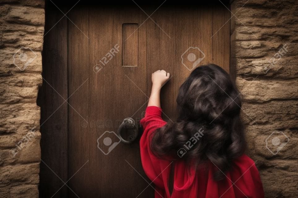 Een jonge vrouw klopt op een oude houten deur.