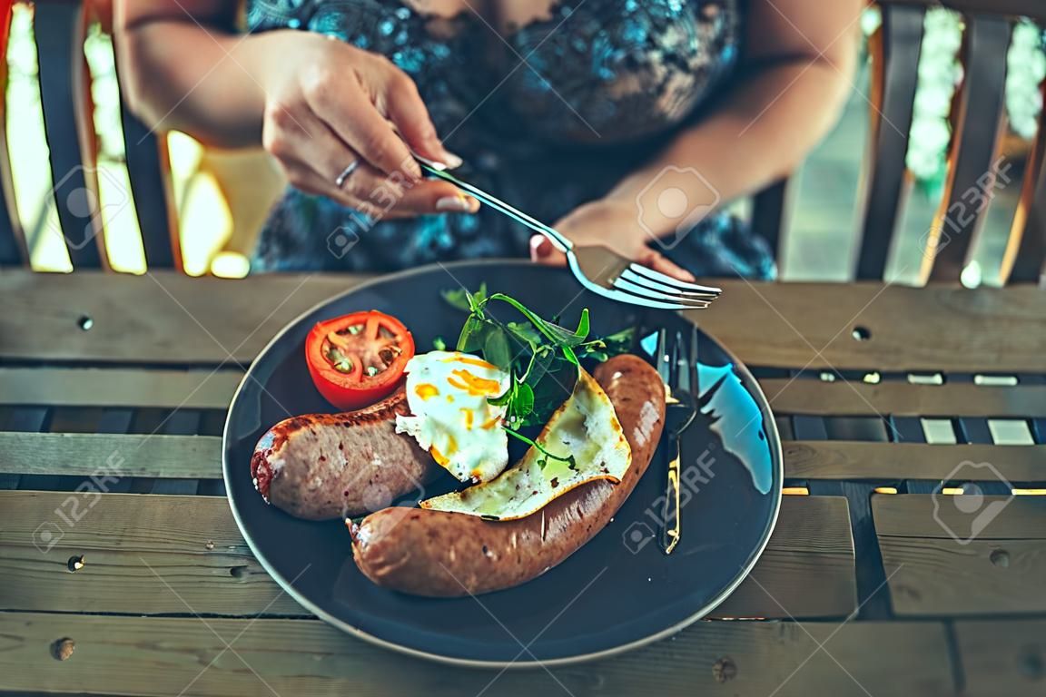 A young woman is having breakfast with sausage in a restaurant outdoors