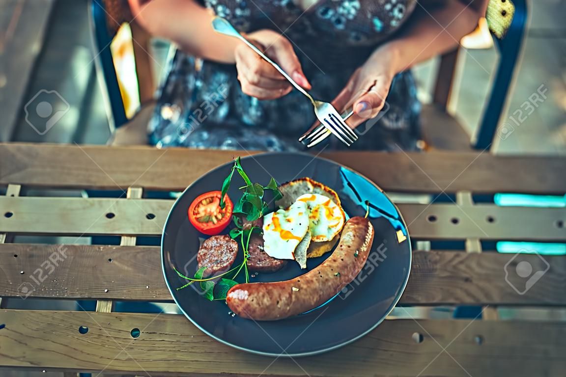 Una joven está desayunando salchichas en un restaurante al aire libre