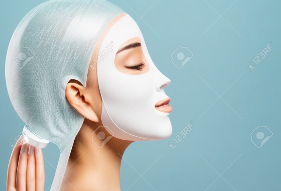 Mujer que aplica una máscara facial de hoja para el tratamiento de su cara. Cierre de tiro, vista lateral.