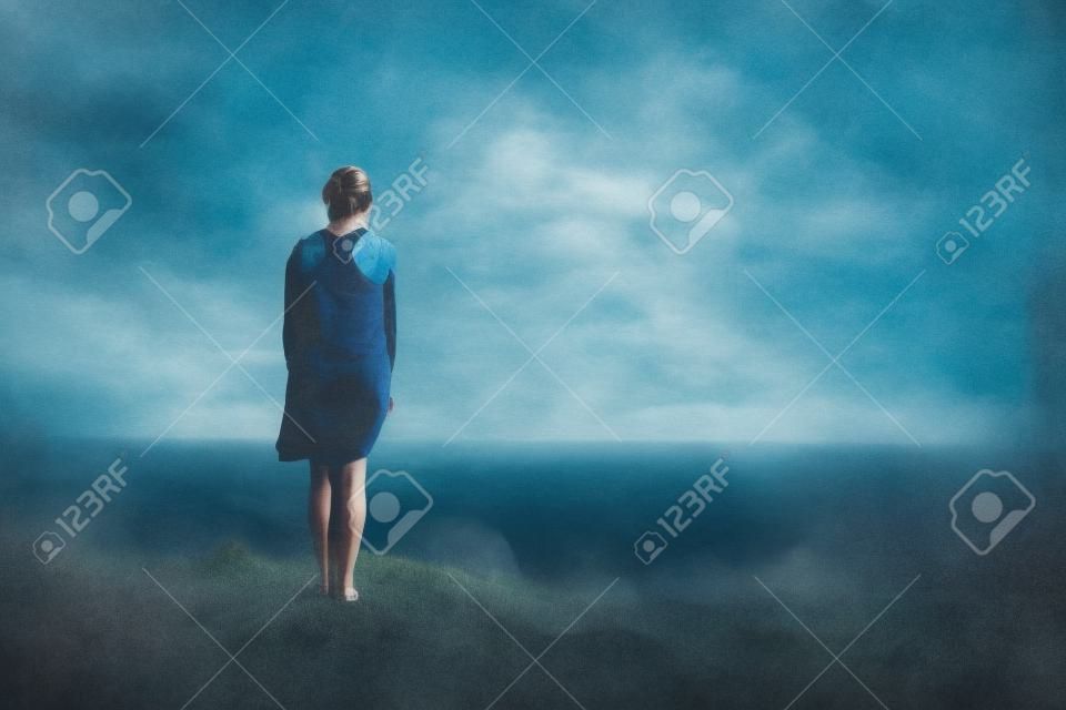 Ontop solitaria mujer pie de una colina en vista del océano.