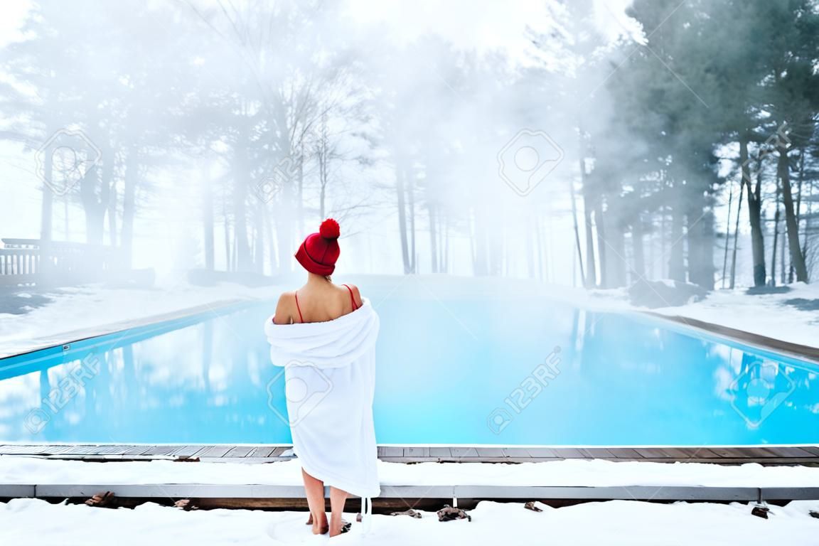 Young blonde woman in bathrobe and red hut near outdoor swimming pool at winter day