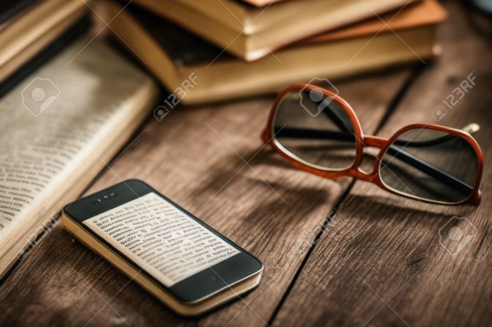 Vecchi libri dell'annata, smartphone e bicchieri su un tavolo di legno