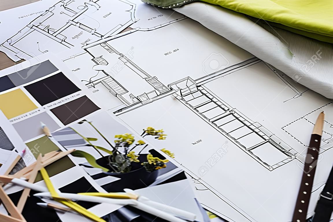Interior designer's working table, an architectural plan of the house, a color palette, furniture and fabric samples in yellow and grey color. Drawings and plans for house decoration.