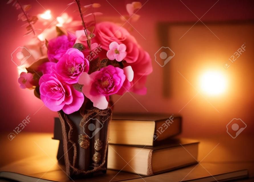 Elegáns csokor rózsaszín virágok és régi könyvek, tabke háttérvilágítással. Vintage dekorációval.