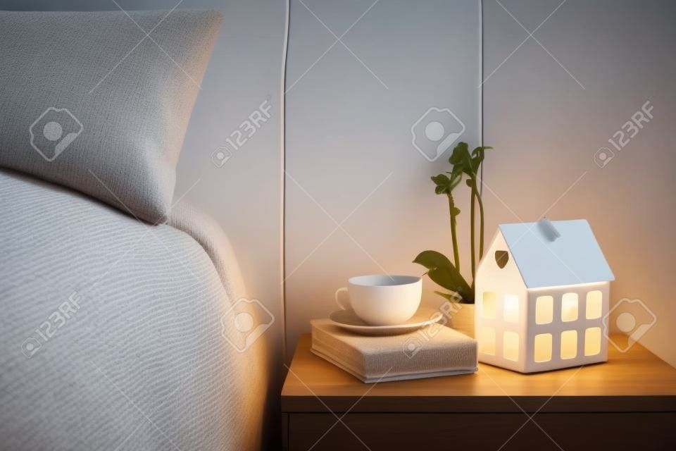 舒適的夜晚臥室內部，一杯茶和放在床頭櫃上夜燈。家庭室內裝飾與溫暖的光。