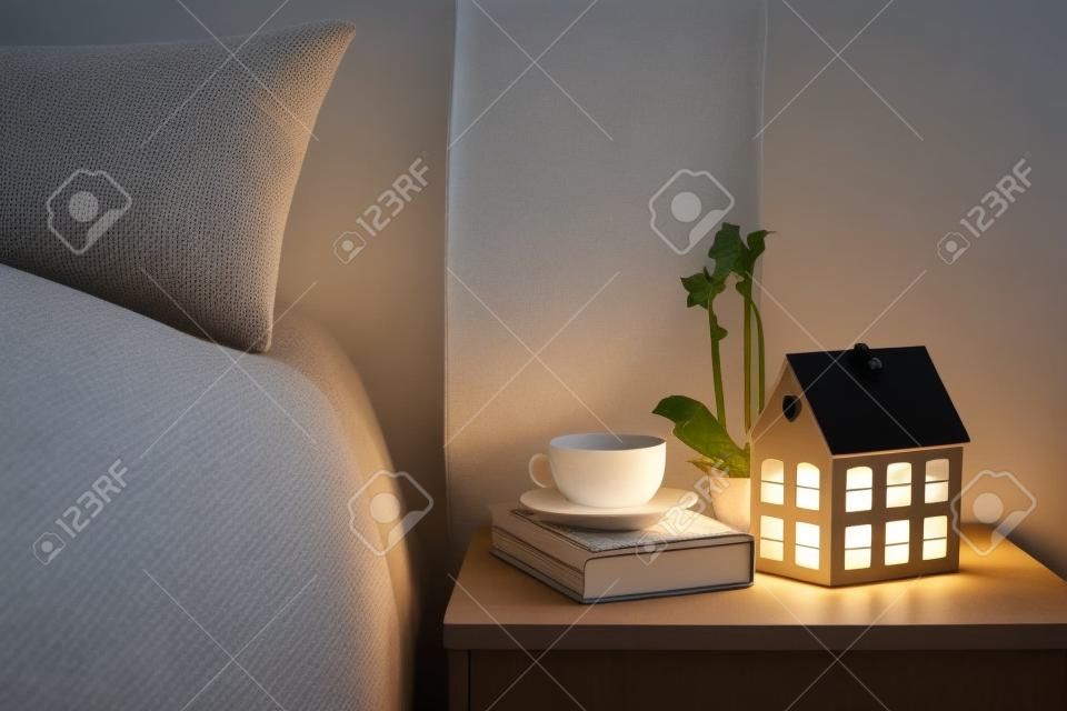 舒適的夜晚臥室內部，一杯茶和放在床頭櫃上夜燈。家庭室內裝飾與溫暖的光。