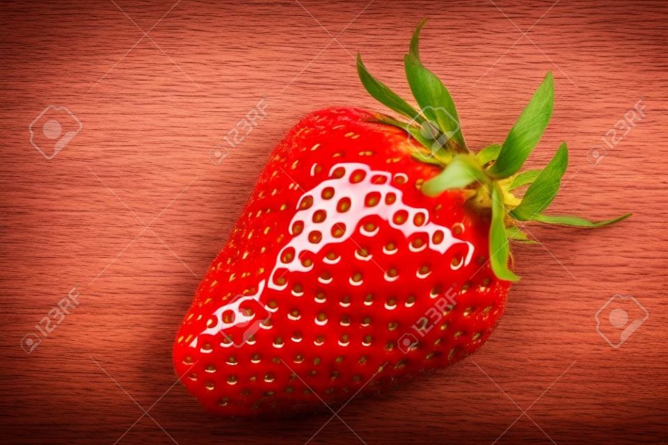 One ripe red organic strawberry on white wooden background