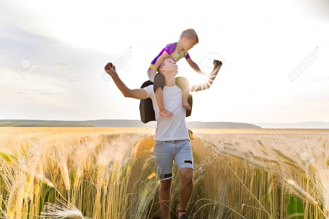 young father with his little son walking in the wheat field at sunset in a warm summer day