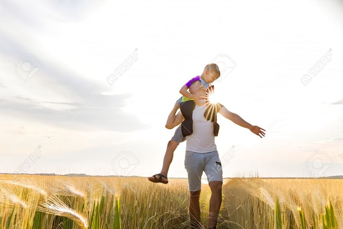 young father with his little son walking in the wheat field at sunset in a warm summer day