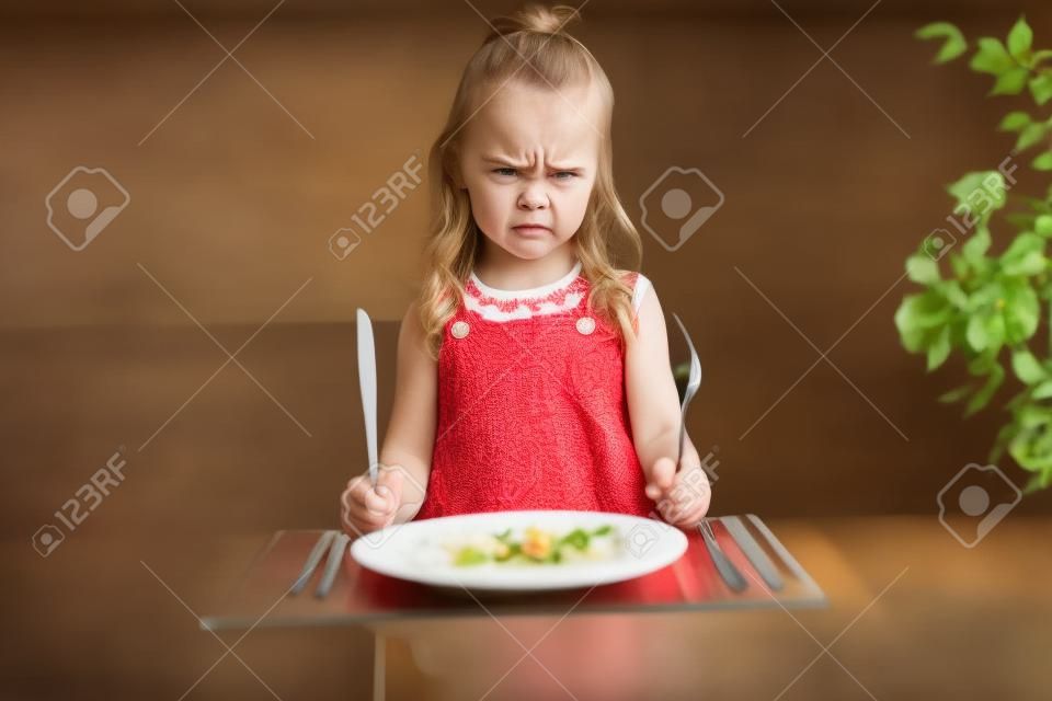 夕食を待っている激怒小さな女の子。フォークを手に持つ